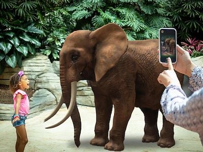 Young girl in front of virtual elephant with woman taking picture on a phone