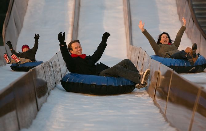 Guests on blue tubes on snow hill lane with hands in the air
