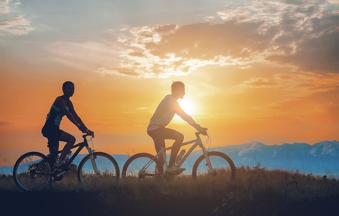 Two people on two mountain bikes by lake at sunset