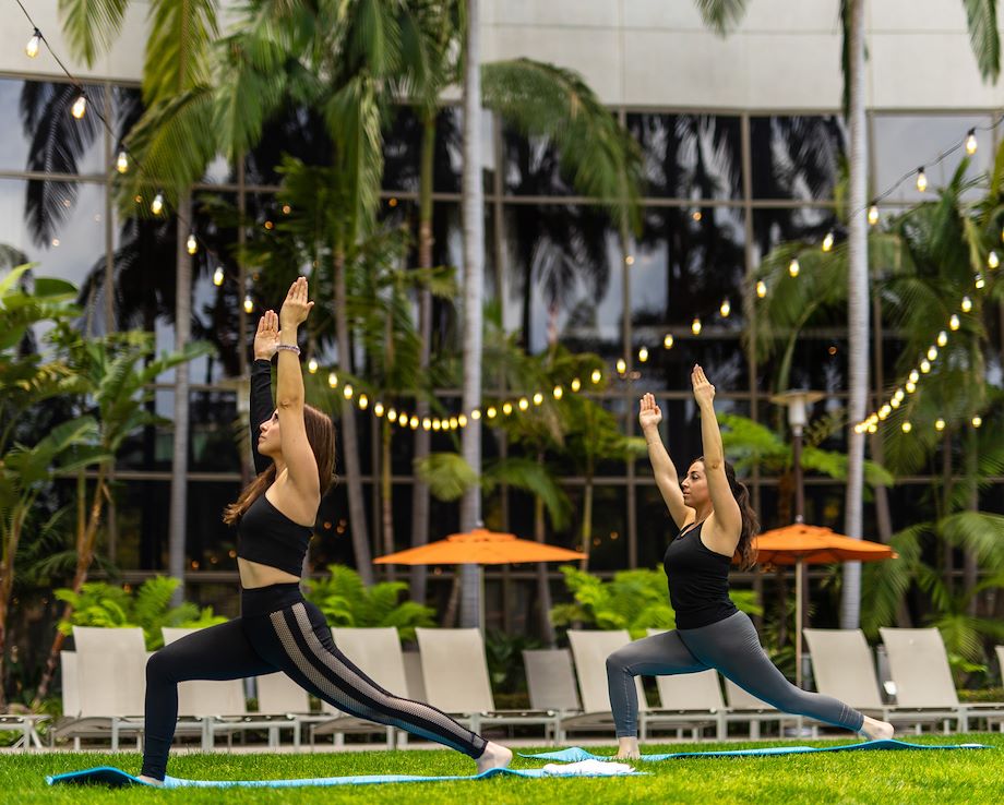 Two women practice yoga on a lawn decorated with strings of lights.