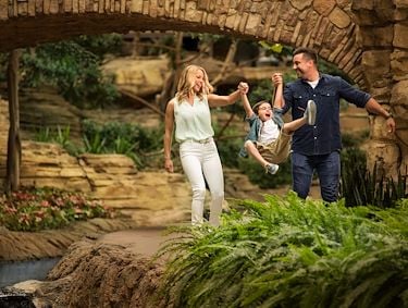 Couple holding hands with child and swinging him between them in atrium gardens at Gaylord Texan