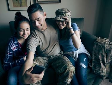 Man in camouflage pants with phone sitting next to two teenage females